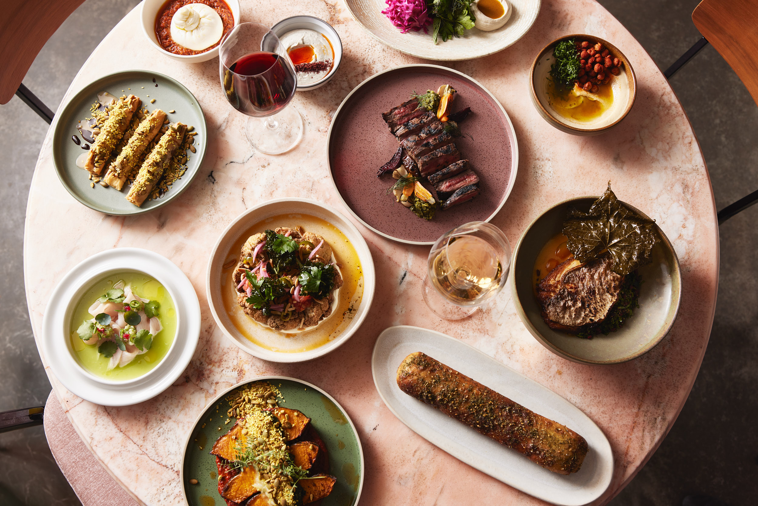 Middle Eastern feast on marble table with meats, salads, hummus, dips, and wine at a Surry Hills restaurant.