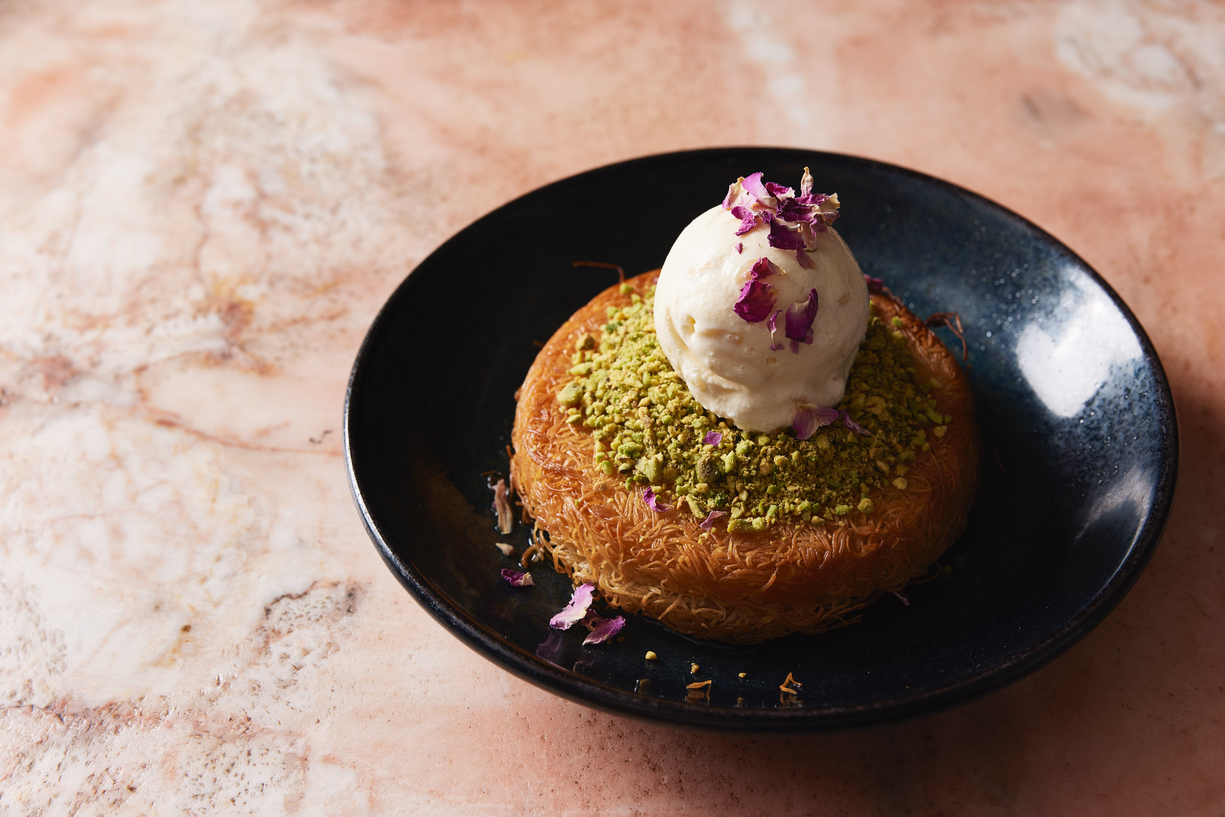 Authentic Middle Eastern knafeh with pistachios, rose petals, and ice cream, served on a marble table in Shaffa Surry Hills.