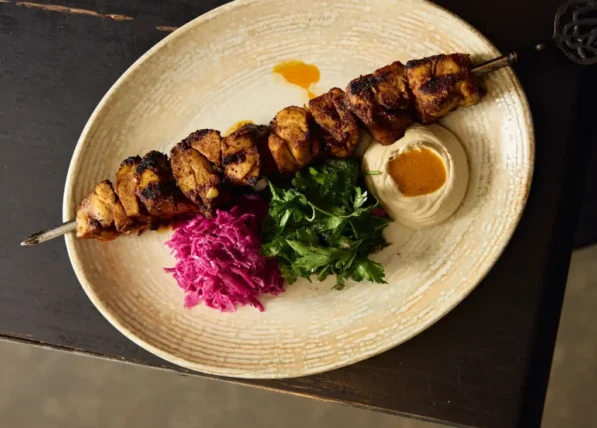 Chicken shawarma skewer with tahini, pickled cabbage, and fresh herbs on a rustic plate – Middle Eastern dining at Shaffa.